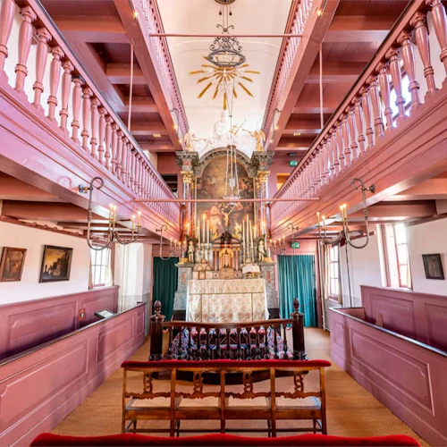 A beautifully ornate chapel interior with a central altar, decorative chandeliers, and wooden pews under a high ceiling.