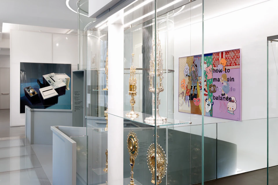 Glass display cases containing ornate metallic artifacts in a modern museum setting, with artwork on the walls.