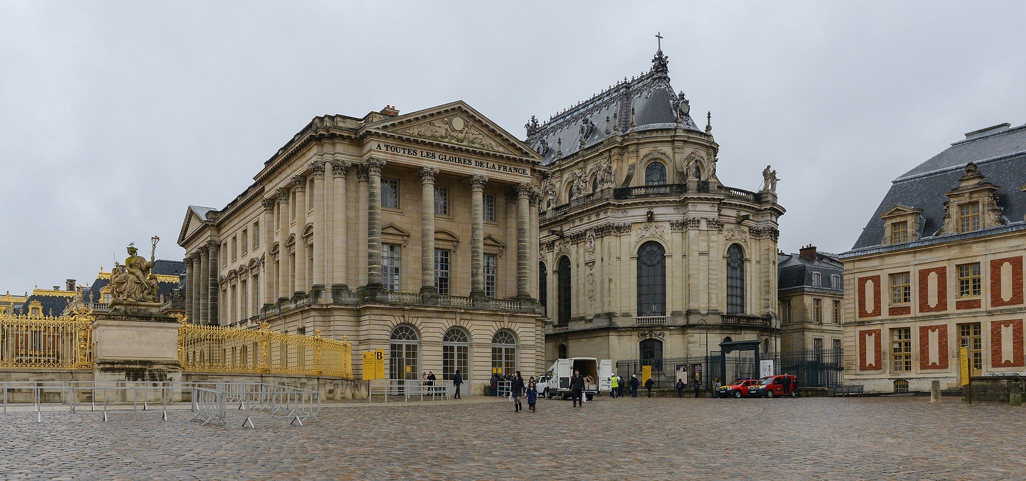 Historic palace complex with statues, a cobblestone courtyard, ornate buildings, gold gates, and a few people walking.