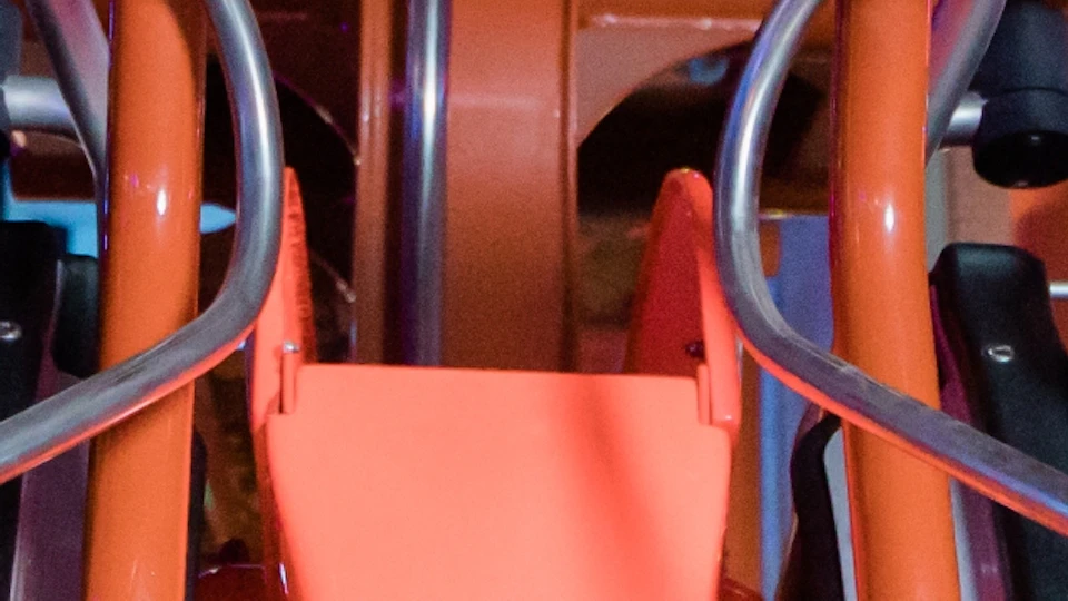 Two people smiling and holding onto handles while seated in an amusement park ride with orange structures.