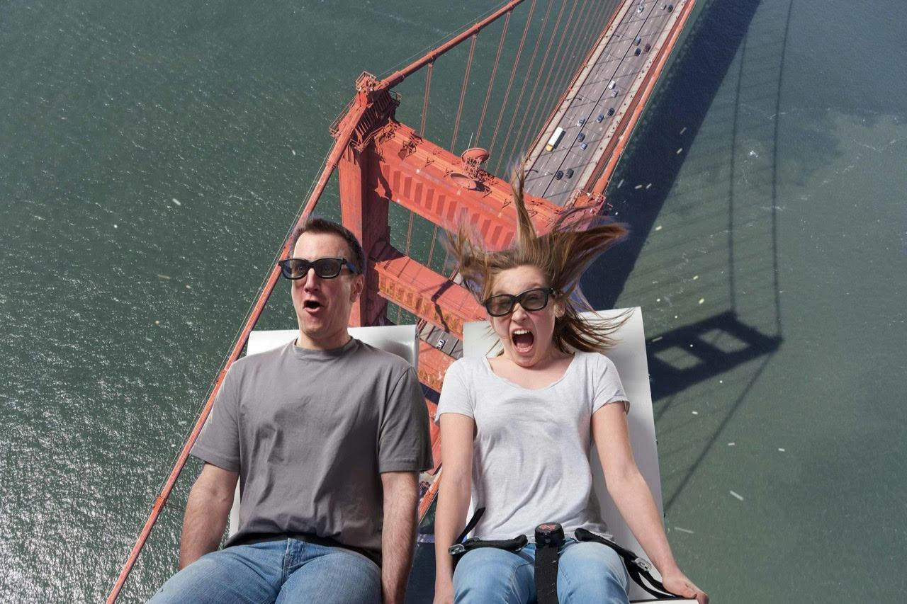 A man and a woman on a ride with a background of the Golden Gate Bridge, both wearing glasses and showing surprised expressions.