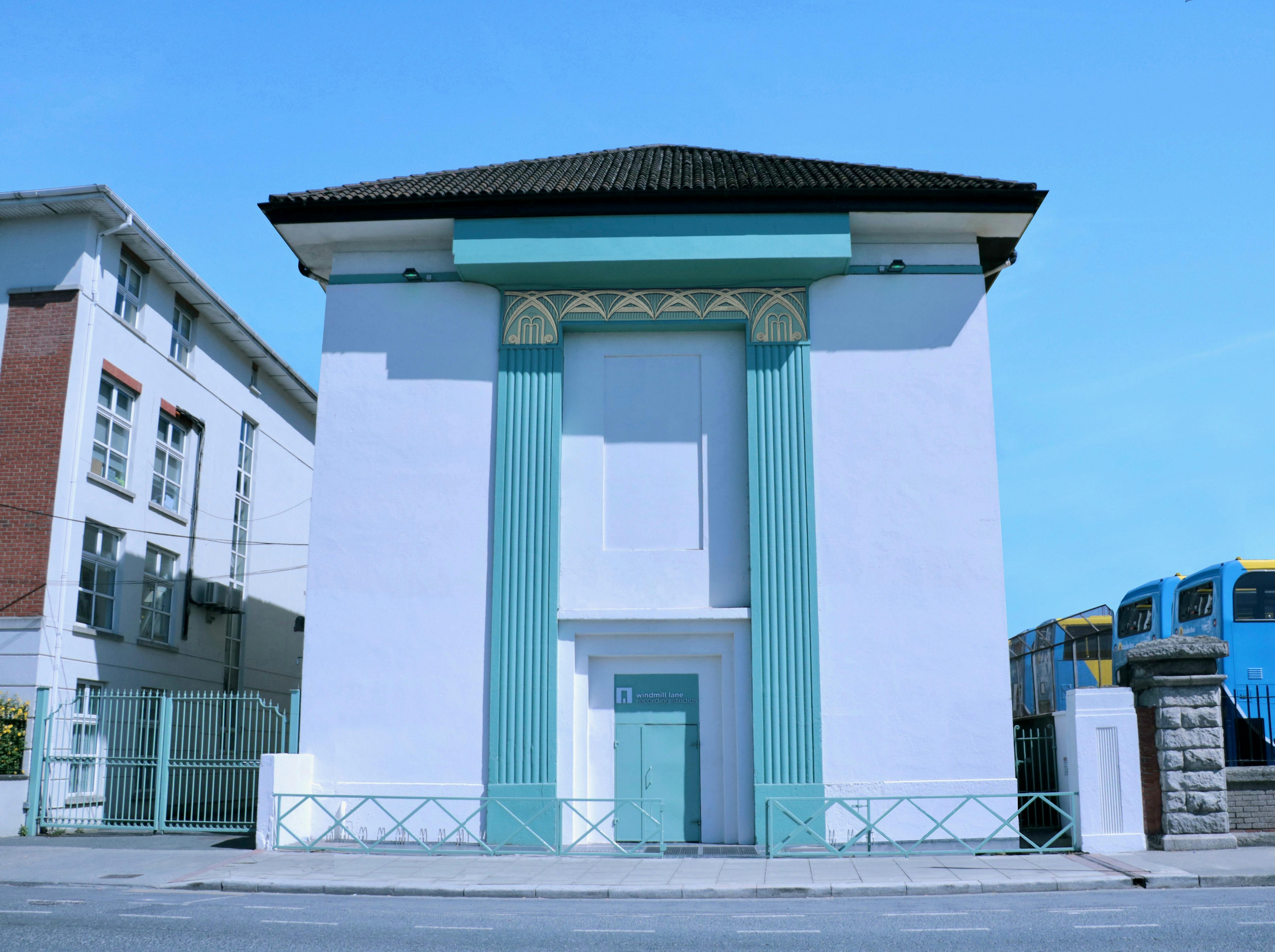 흰색 복층 건물과 2층 버스 사이에 청록색 장식 기둥과 문이 있는 흰색 건물입니다.