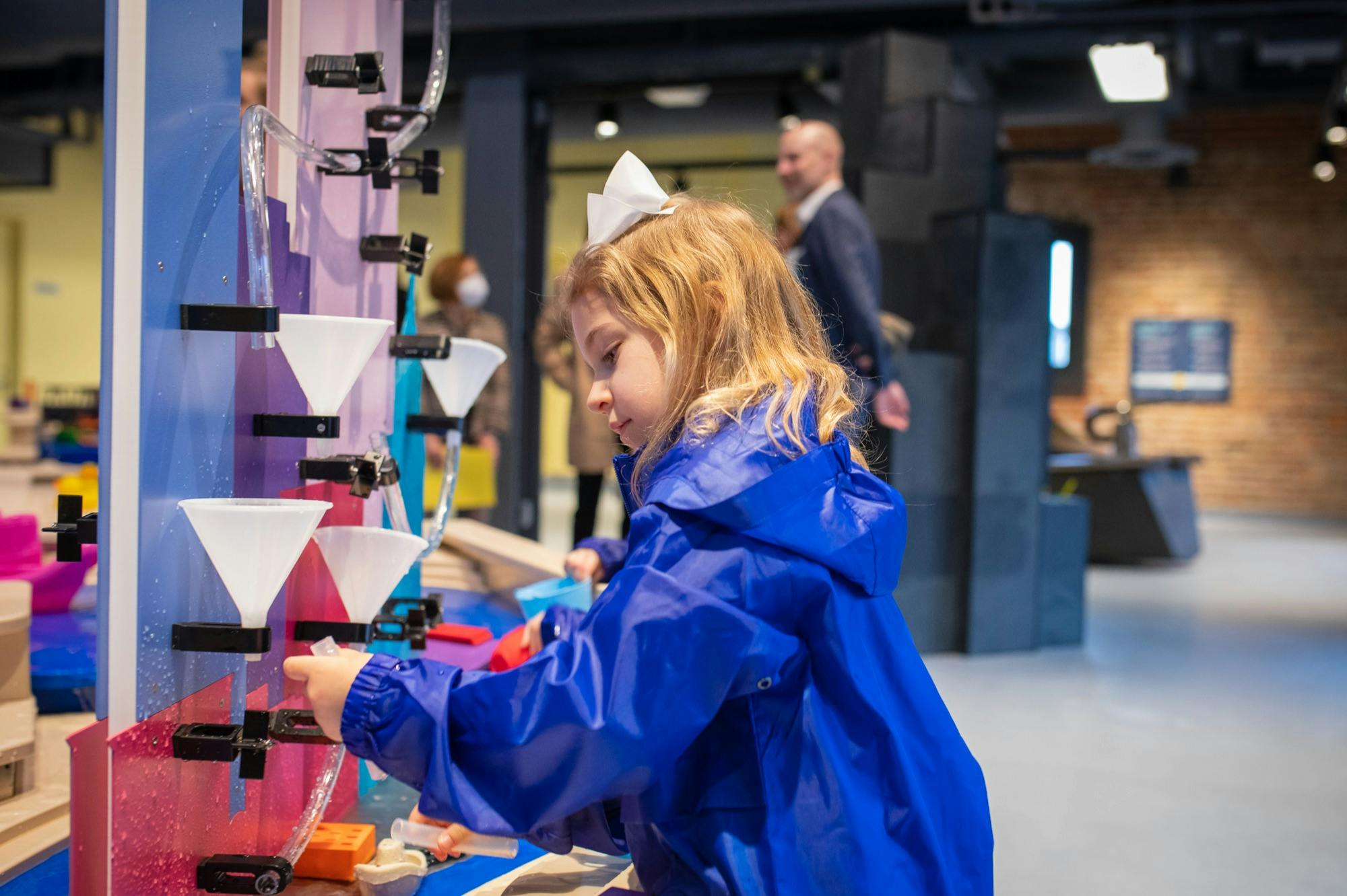 A child wearing a blue jacket interacts with an interactive exhibit in a museum, with other visitors in the background.