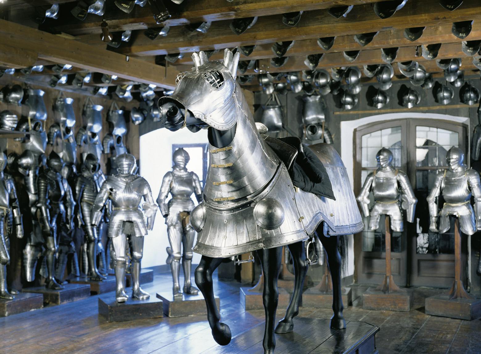 A museum room filled with medieval armor displays, including a knight on a horse and various suits of armor on mannequins.