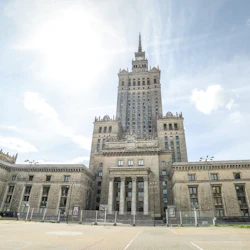 Hög, utsmyckad byggnad med en spetsig spiral en solig dag, flankerad av två symmetriska vingar, står på en tom, asfalterad innergård.