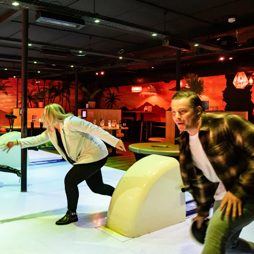 Fyra personer i en bowlinghall bowlar aktivt, med en tropisk väggmålning i bakgrunden.