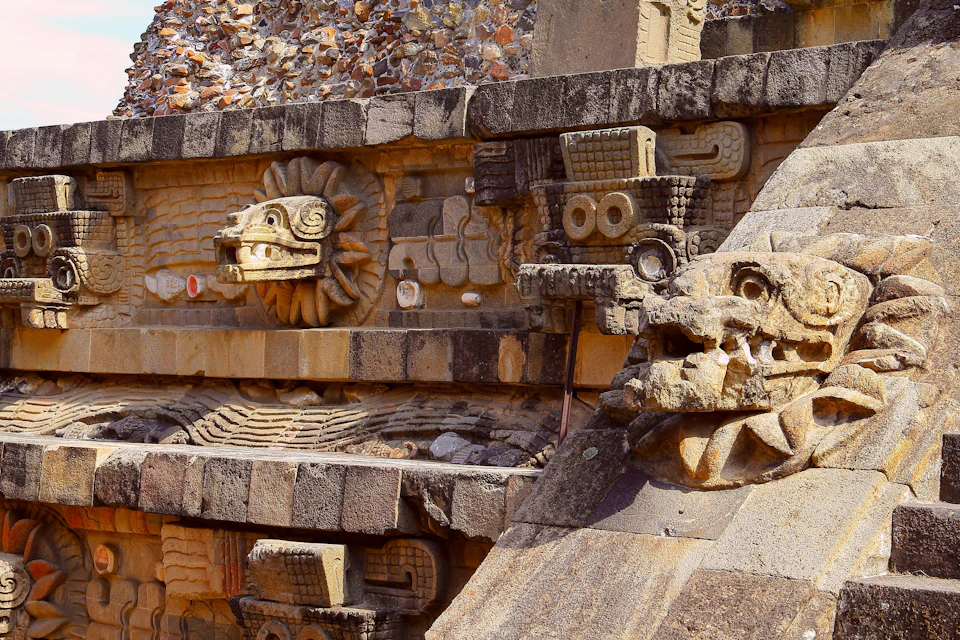 Stone carvings on an ancient wall, featuring stylized serpents and geometric patterns, partially worn by time.
