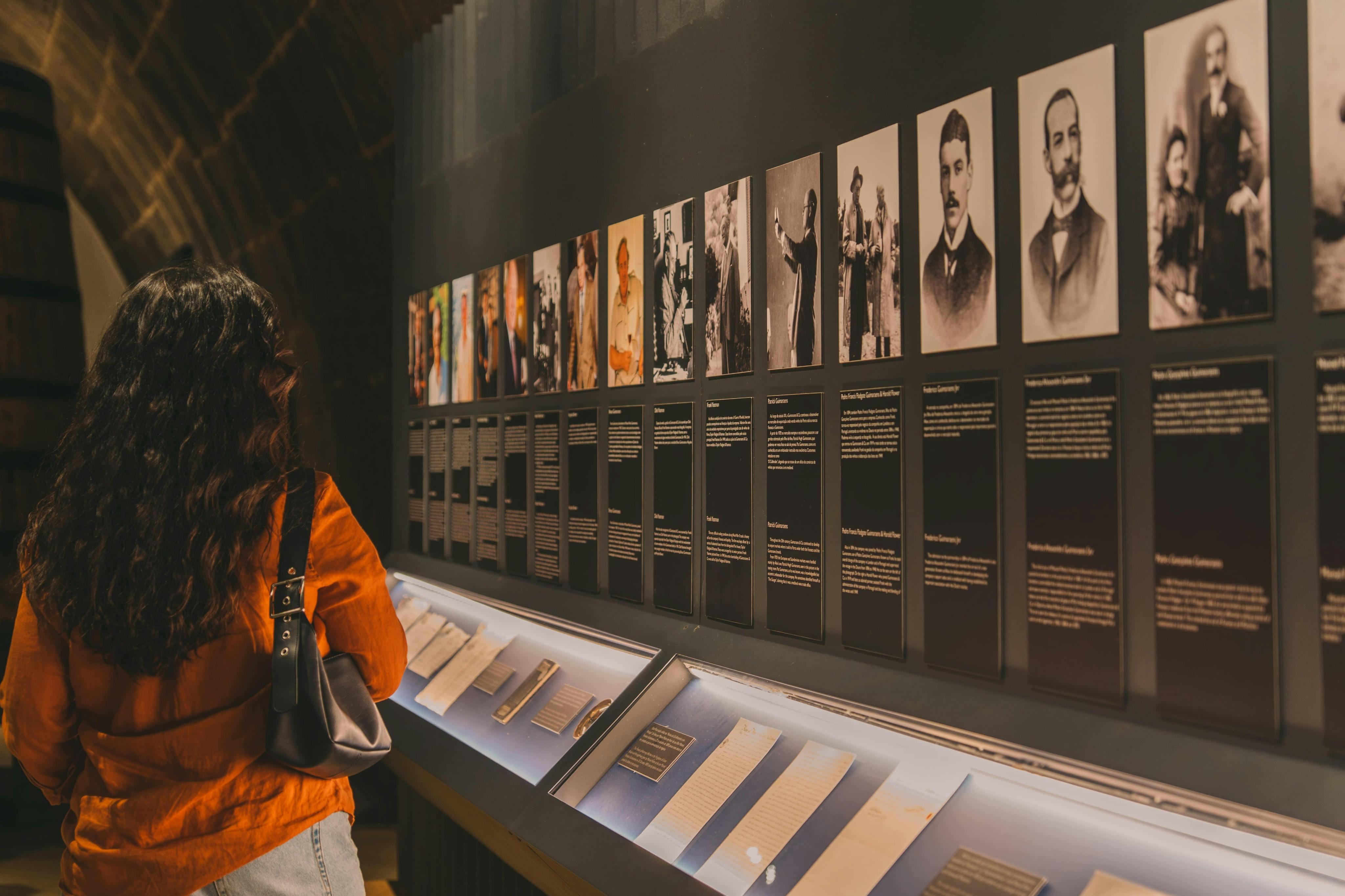 A person in an orange jacket views a museum exhibit with photographs and descriptive plaques above a display case of documents.