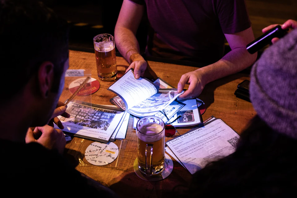 Several people sitting at a wooden table with documents and beer glasses, interacting and discussing the papers.
