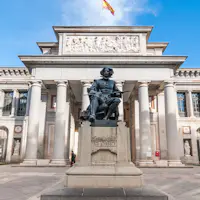 Estátua de Diego Velázquez em frente às colunas do Museu do Prado, com uma bandeira espanhola hasteada por cima.