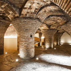 En välvd, tegelvalvad underjordisk kammare med upplyst stengolv och flera tegelpelare.