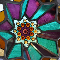 Färgglatt glasmålningsfönster med ett symmetriskt stjärnmönster i lila, grönt, orange och gula nyanser.
