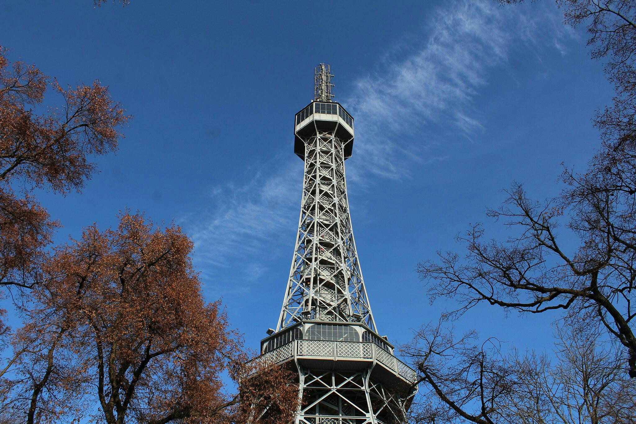 Tall metal observation tower surrounded by trees with autumn foliage, set against a clear blue sky.