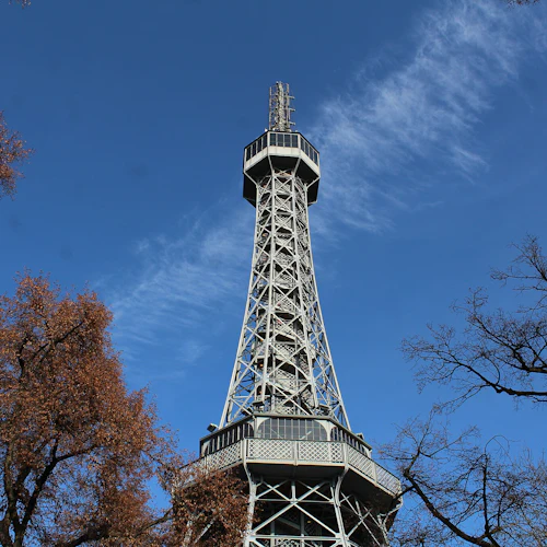 Högt metalltorn omgivet av träd med höstlövverk, mot en klarblå himmel.
