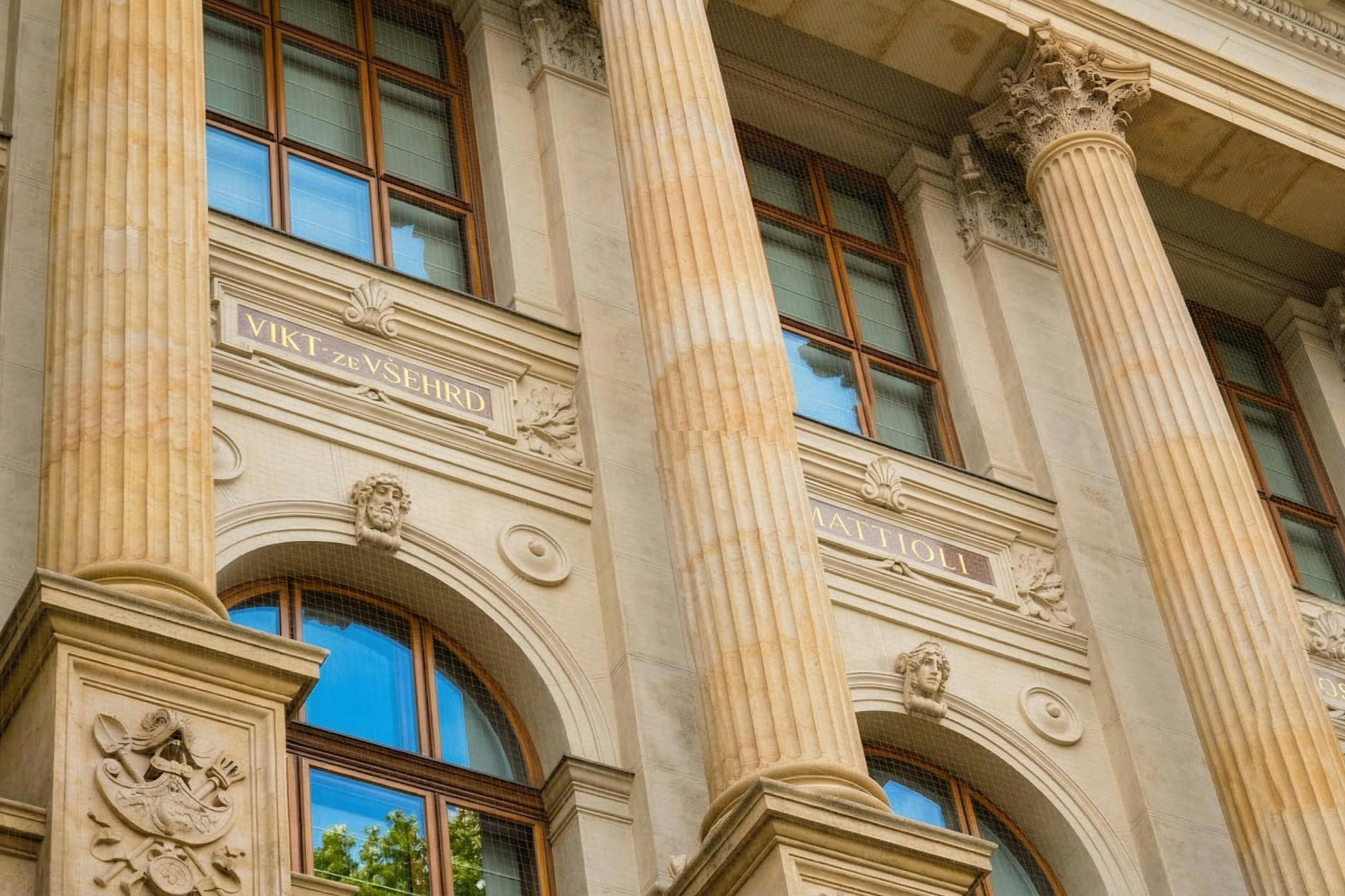 화려한 기둥, 아치형 창문, 장식 디테일이 돋보이는 고전적인 건물의 정면에는 이름과 조각이 있습니다.