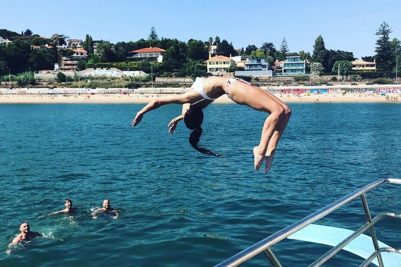 A young woman performing a backflip from a diving board during a boat party in Lisbon.