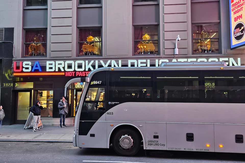 The tour departs in a luxury bus from just off Times Square , outside the Brooklyn Deli