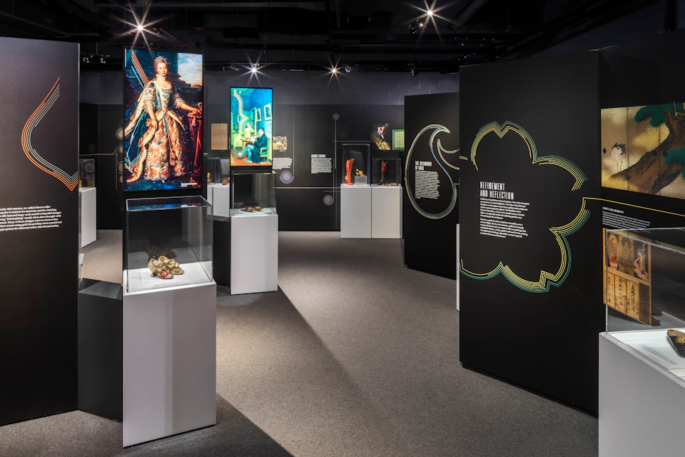 Museum exhibit with paintings, informational text, artifacts in display cases, and spotlights highlighting the displays.