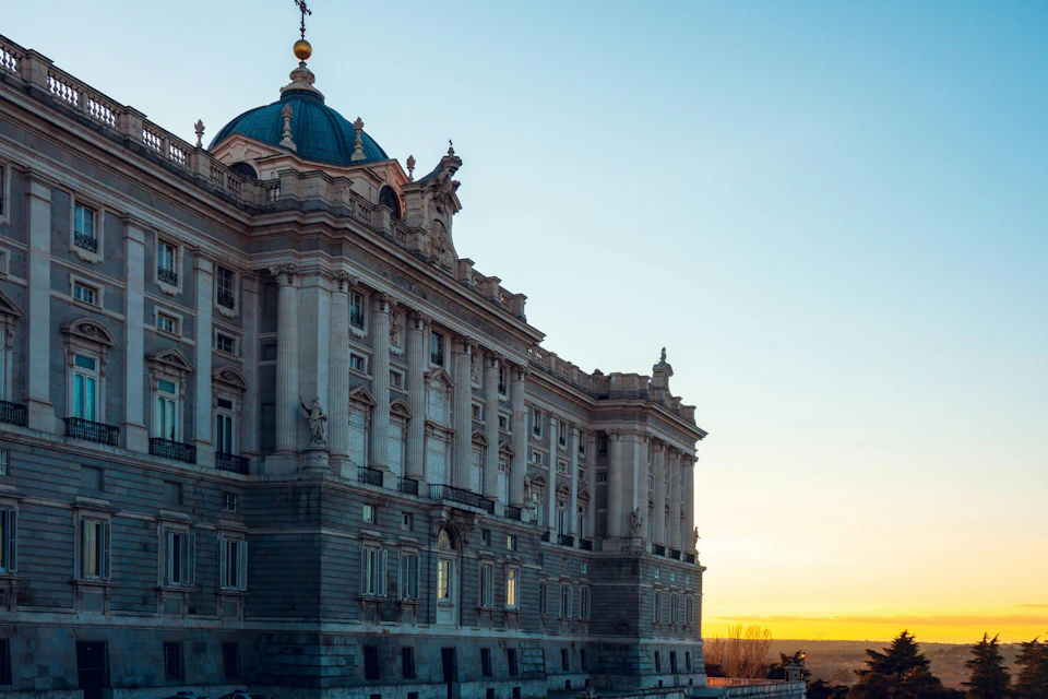 Large historic building with ornate architecture and a blue dome, set against a sunset sky.