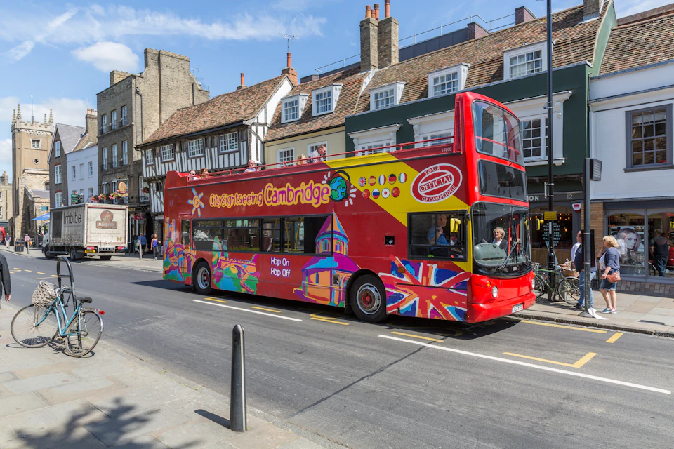 A colorful double-decker sightseeing bus labeled "City Sightseeing Cambridge" on a street lined with old buildings.