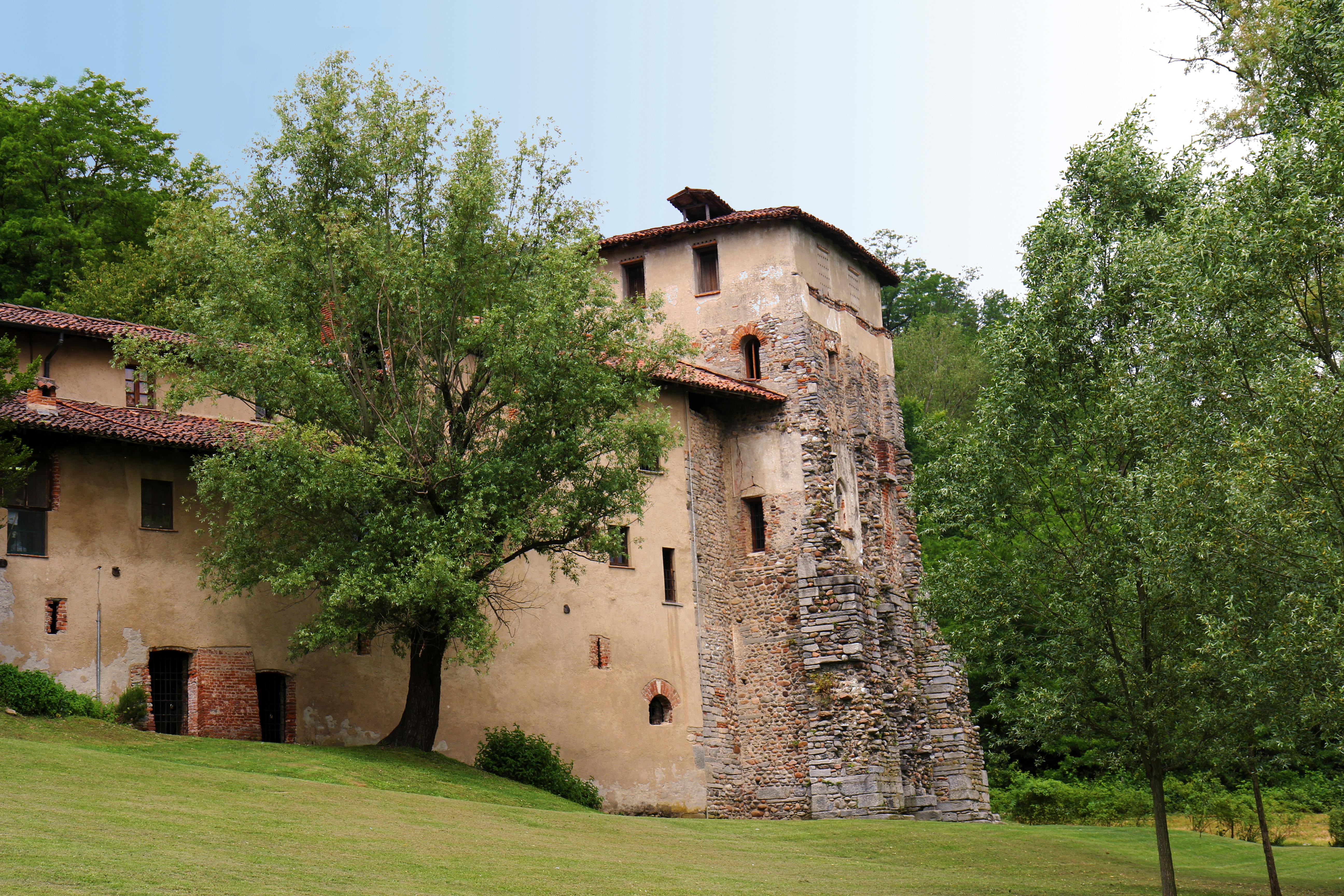 古老的石头建筑，屋顶铺有瓷砖，在晴朗的日子里，周围环绕着树木和绿色植物。