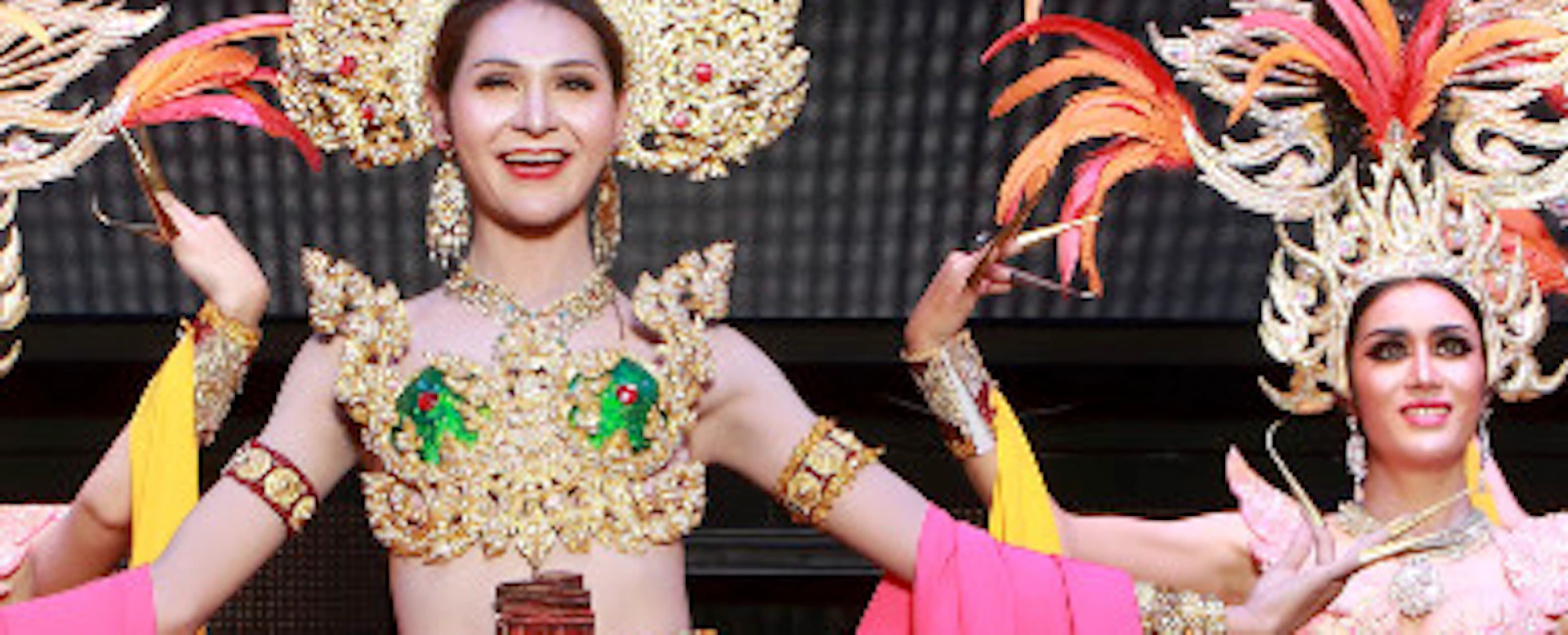 Four performers in ornate costumes with feathered headdresses and flowing fabrics, dancing on stage.