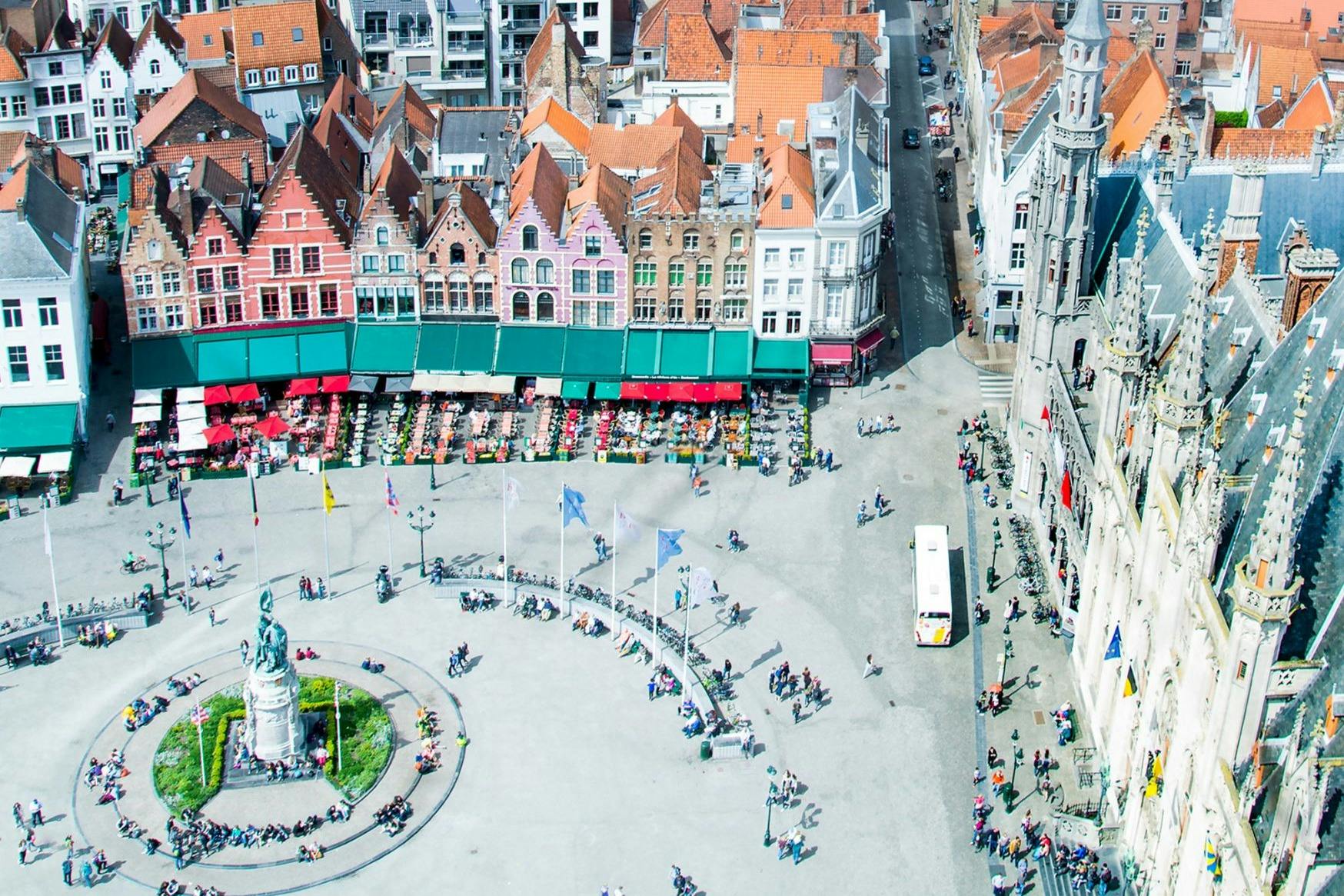 大型繁忙的广场鸟瞰图，广场上有雕像、旗帜和人物。 色彩缤纷的建筑，红色屋顶，后面有户外座椅。