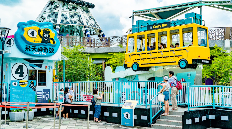 A yellow amusement park ride shaped like a bus, labeled 'Crazy Bus,' with people aboard and others observing below.