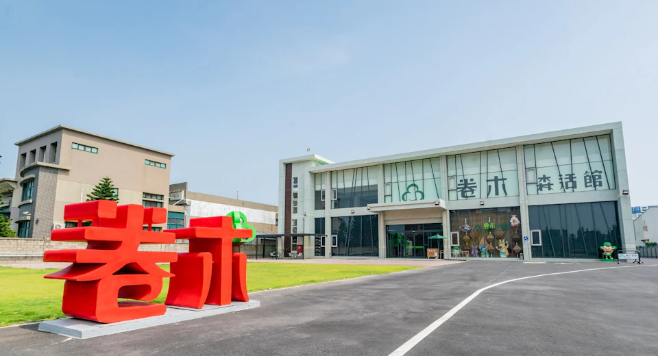 A modern building with large windows, a red sculpture in the foreground, and a clear blue sky above.