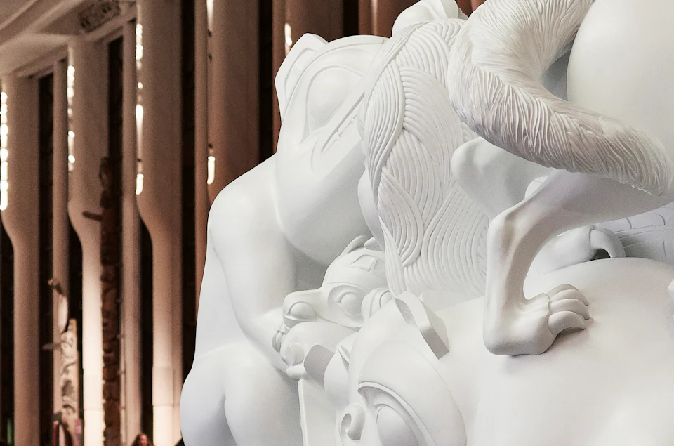 A family observes a large, detailed white sculpture in a modern museum with tall columns and large windows.