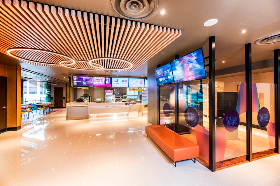 Modern fast-food restaurant interior with a counter, menu screens, orange bench seating, and decorative ceiling design.