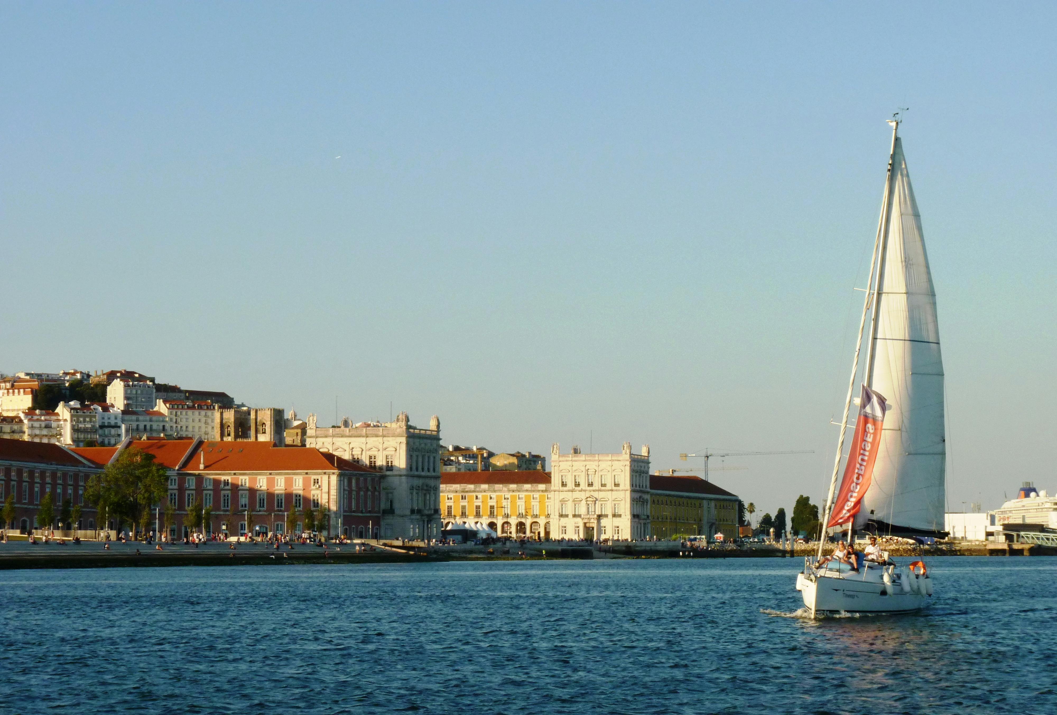 カラフルな歴史的建造物、右側にセーリングボート、夕暮れ時には穏やかな青空が広がるウォーターフロントのシーン。