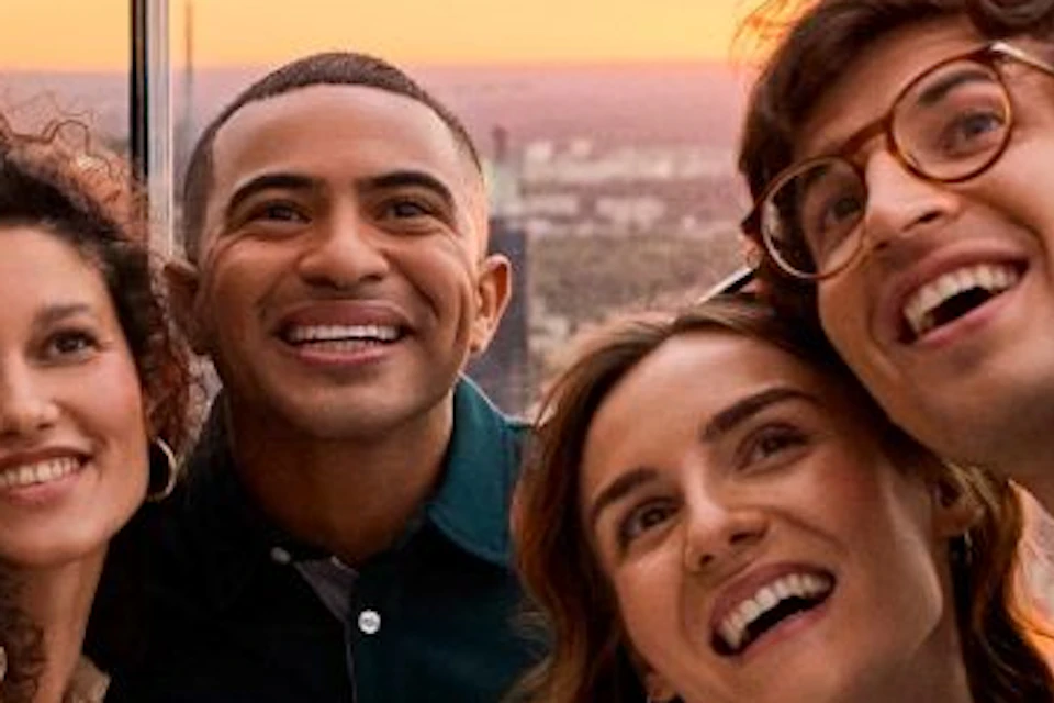 Four people taking a selfie on a rooftop at sunset, with a cityscape visible in the background.
