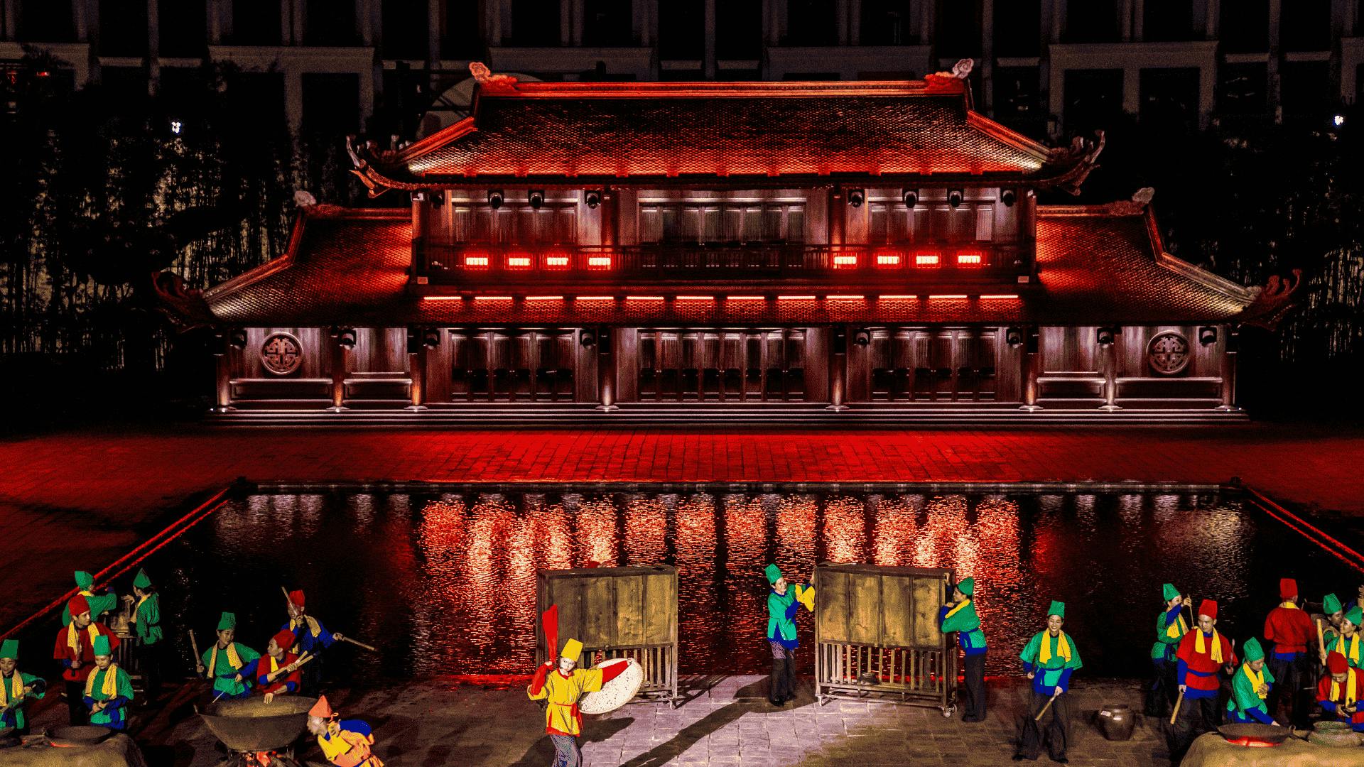 A nighttime stage performance in front of an illuminated traditional building with performers in colorful costumes.