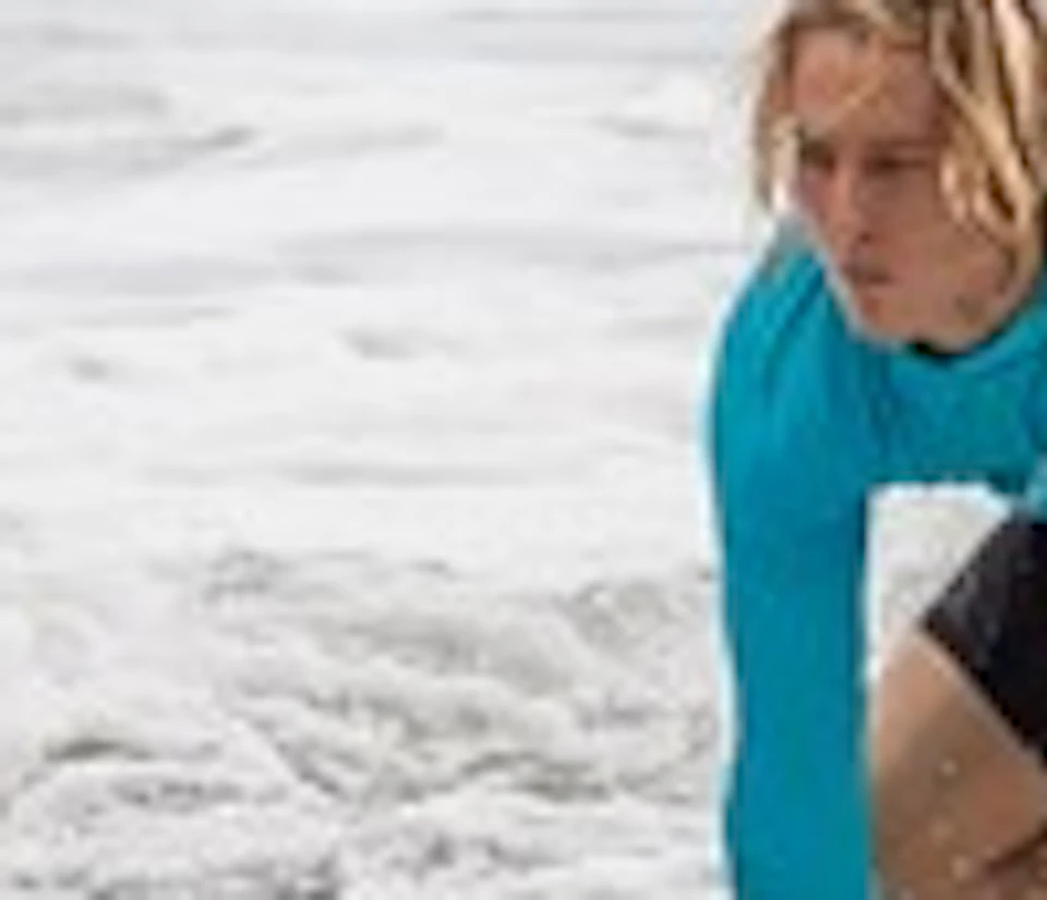 Three people in blue wetsuits are surfing small waves on blue surfboards in the ocean.