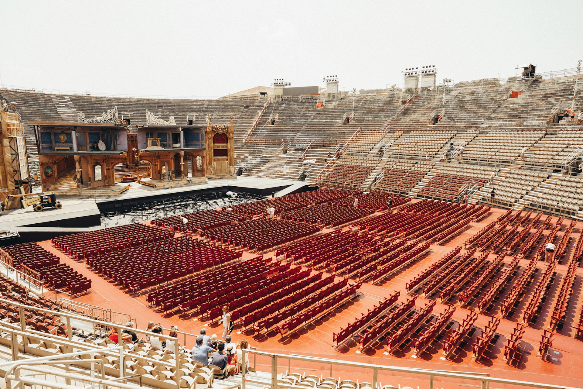 A large, empty amphitheater with rows of red chairs facing an elaborate stage. Few people are scattered in the seating area.