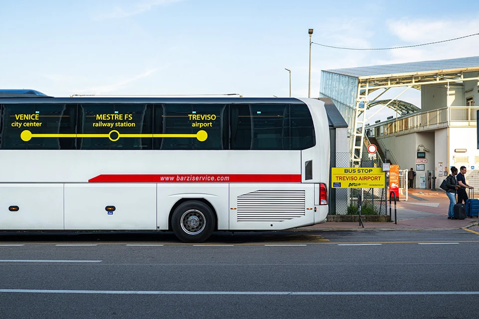A white bus parked at a bus stop with yellow signs indicating destinations to Mestre FS railway station and Treviso airport.