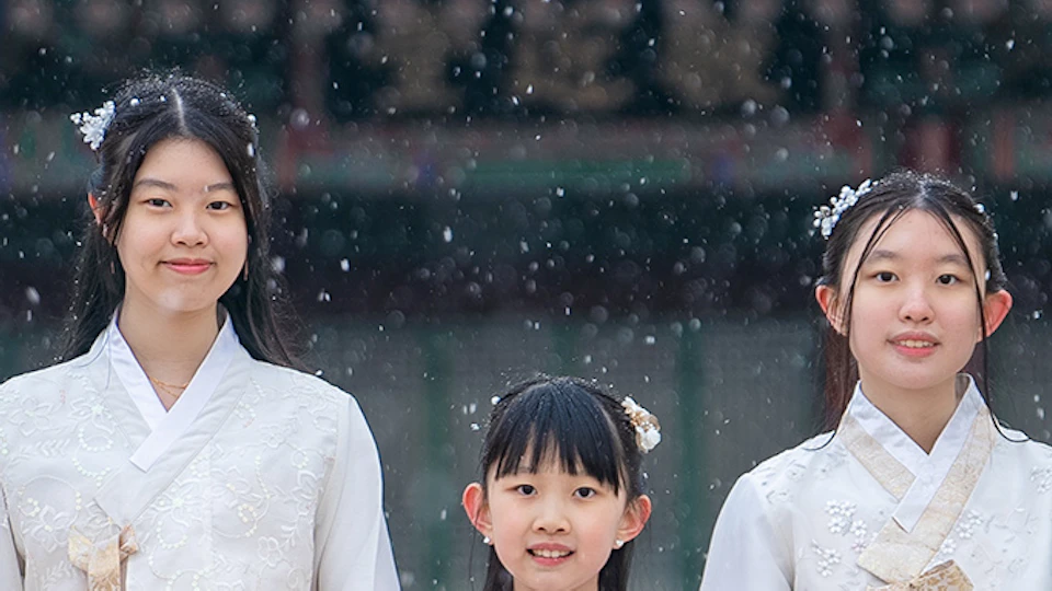 A group of people wearing traditional Korean hanbok outfits with intricate designs, standing outdoors in a snowy setting.