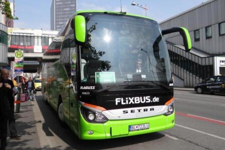 一辆绿色和黑色的FlixBus停在城市街道上，前挡风玻璃上可以看到司机。