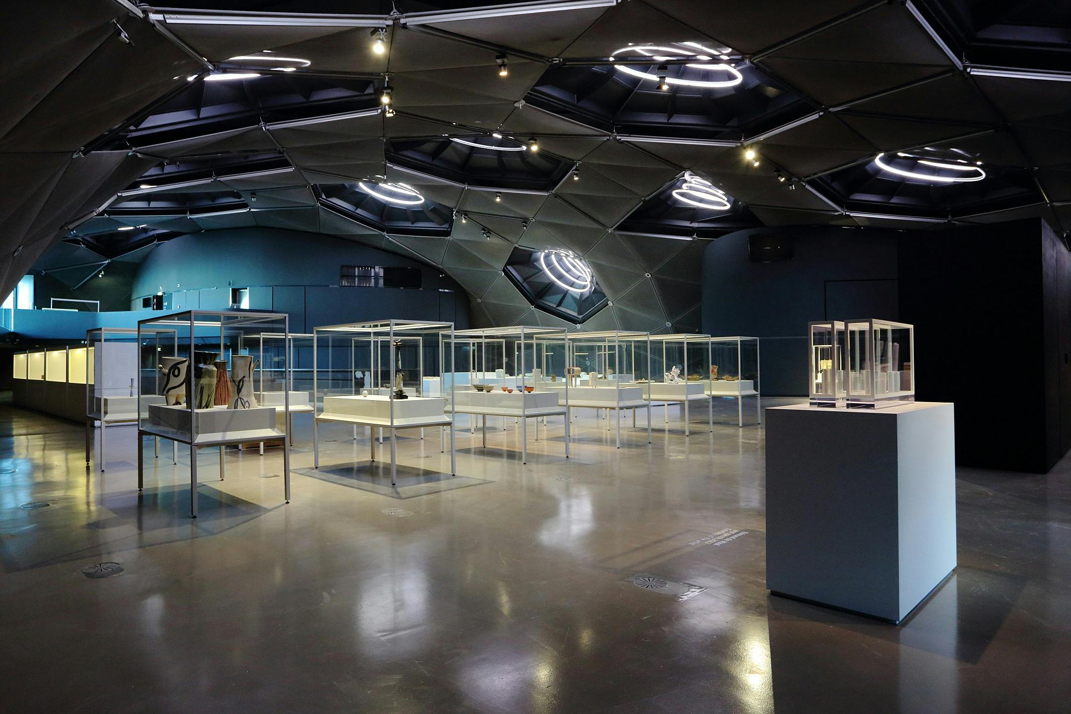 现代化的展厅，几何形状的天花板，装有文物的照明展示柜，抛光混凝土地板。