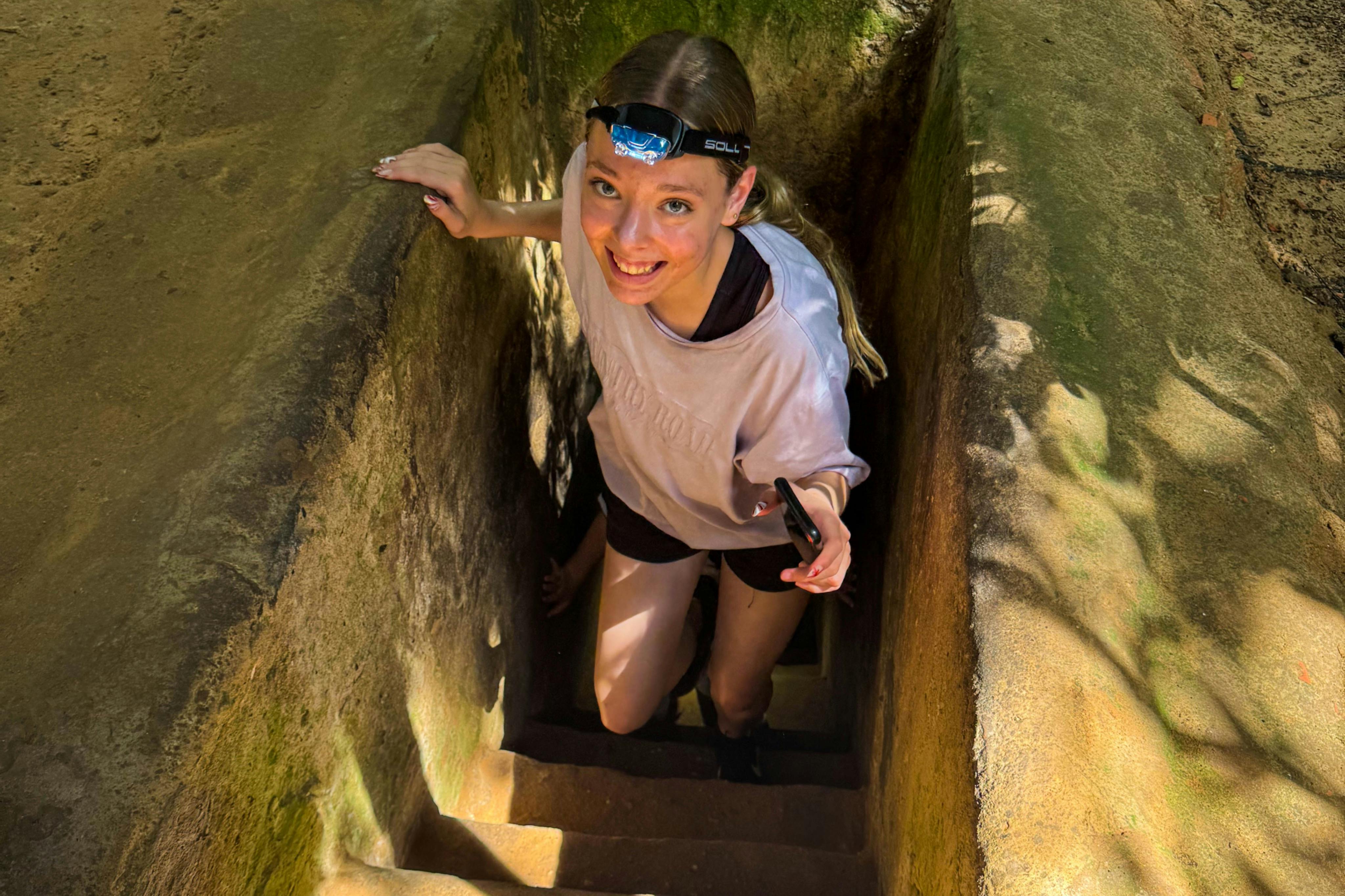 Při stoupání po úzkých kamenných schodech obklopených mechovými zdmi se usmívá osoba s čelovkou.