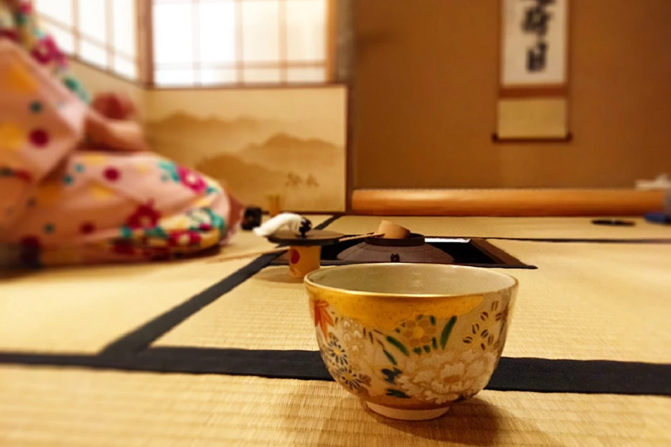 A ceramic tea bowl with floral designs on a tatami mat in a traditional Japanese room.