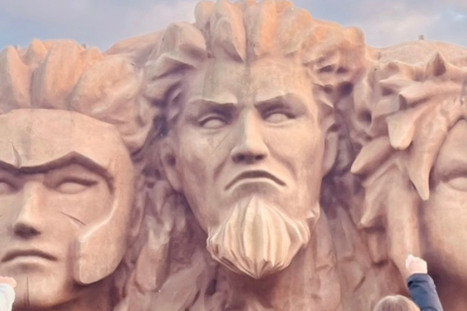 A group of people facing a large stone relief featuring four stylized faces, with an exit sign visible in the background.