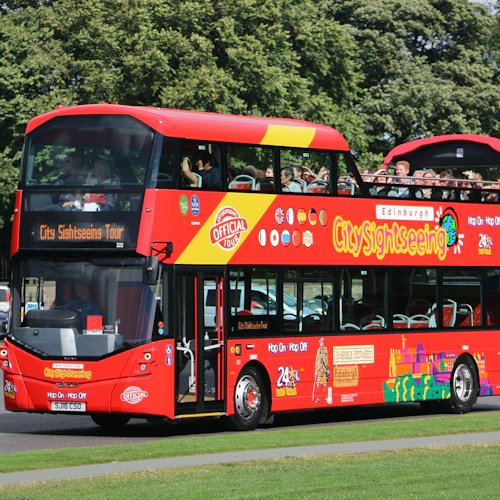 Röd dubbeldäckad sightseeingbuss med "CitySightseeing" -märkning och turister på det öppna övre däcket, med träd i bakgrunden.