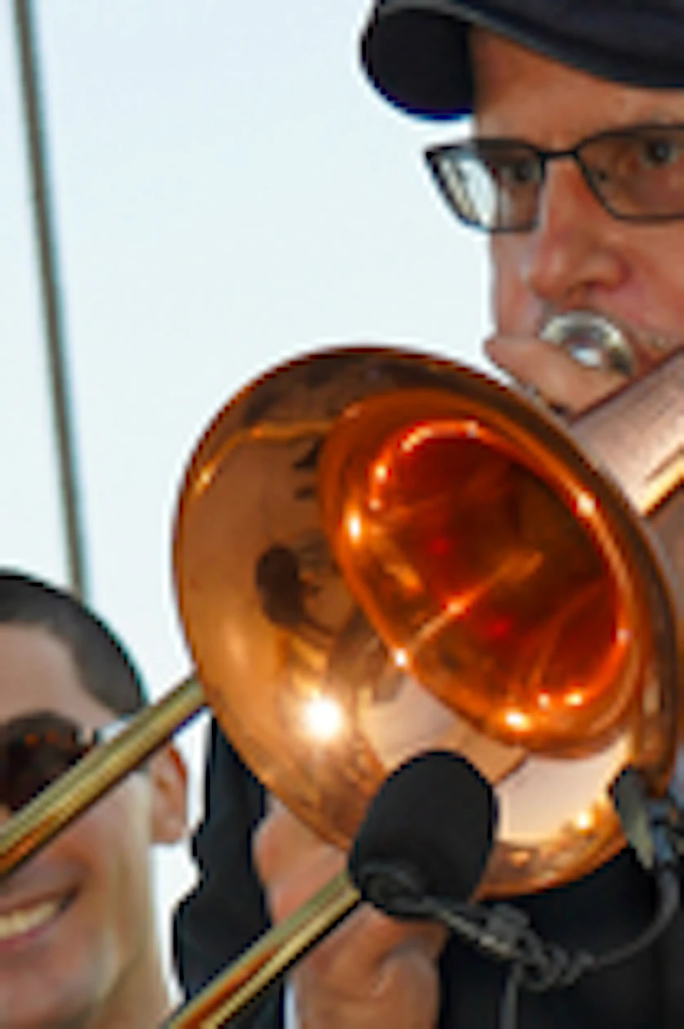 Two musicians playing brass instruments on the deck of a sailing ship, with sails and ropes visible in the background.