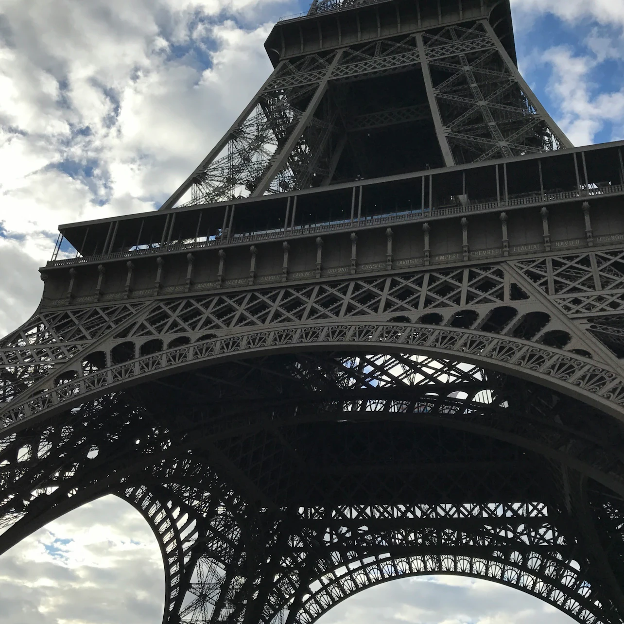 Close-up view of the Eiffel Tower from below, showing its intricate iron lattice structure against a partly cloudy sky.