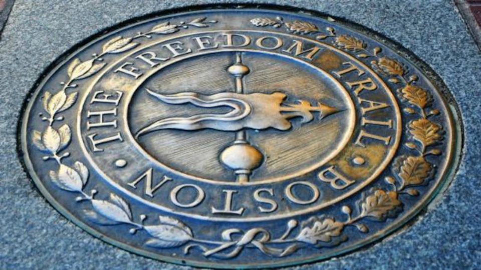 Bronze plaque embedded in pavement, inscribed with "The Freedom Trail Boston," adorned with leaf and berry motifs.