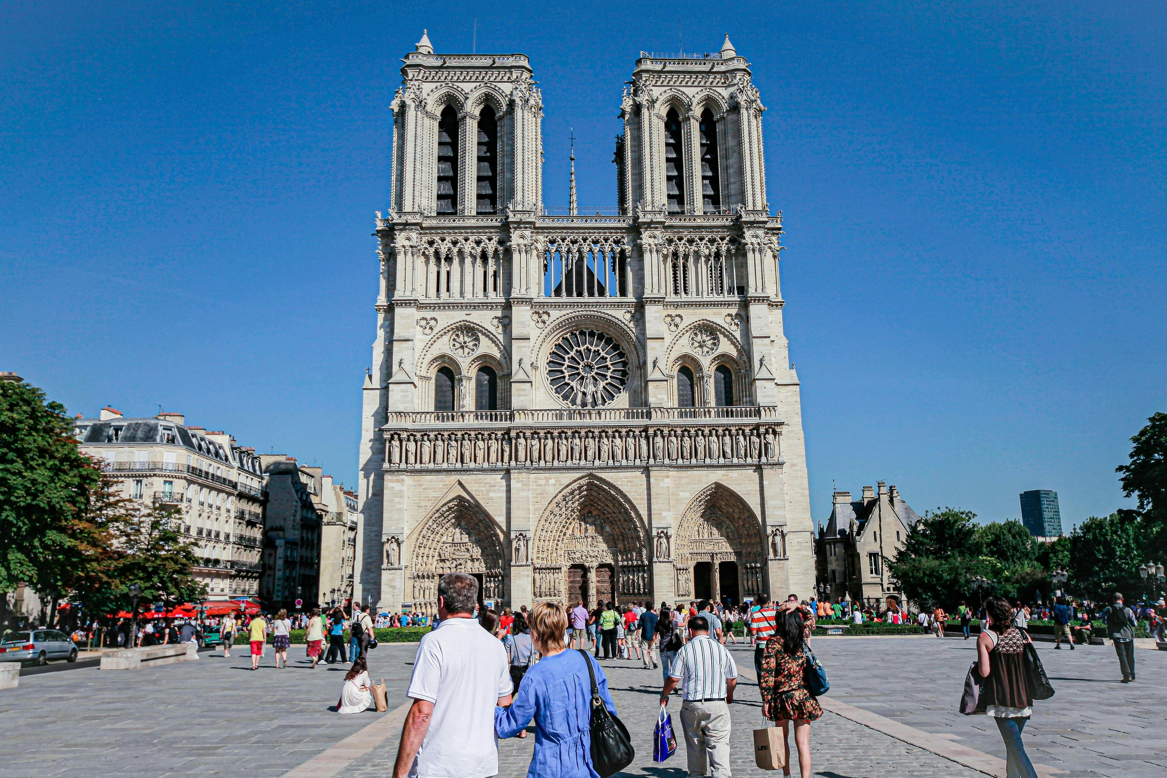 People walking and gathering in front of a large, historic cathedral under a clear blue sky.