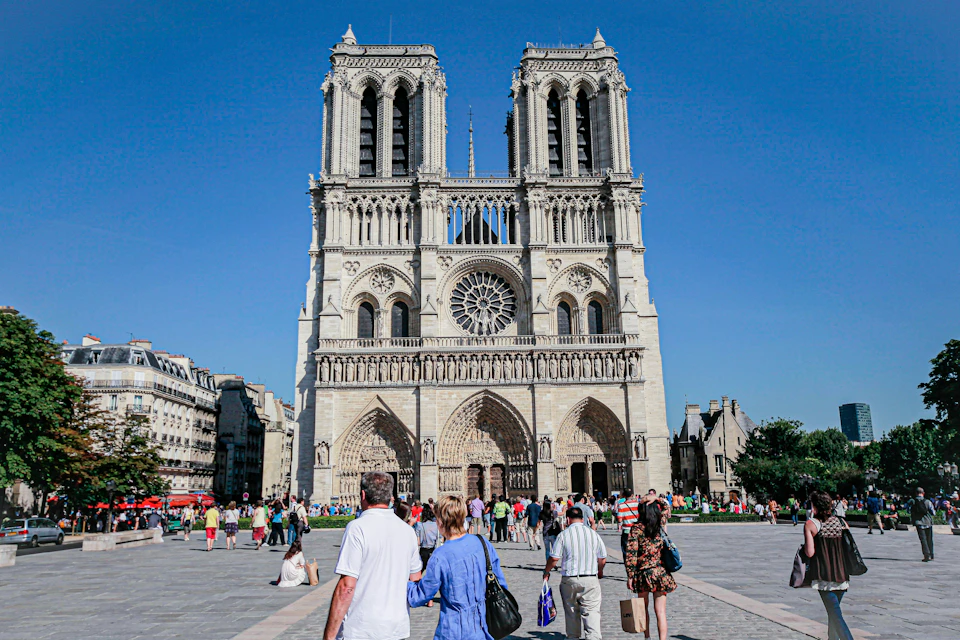 People walking and gathering in front of a large, historic cathedral under a clear blue sky.
