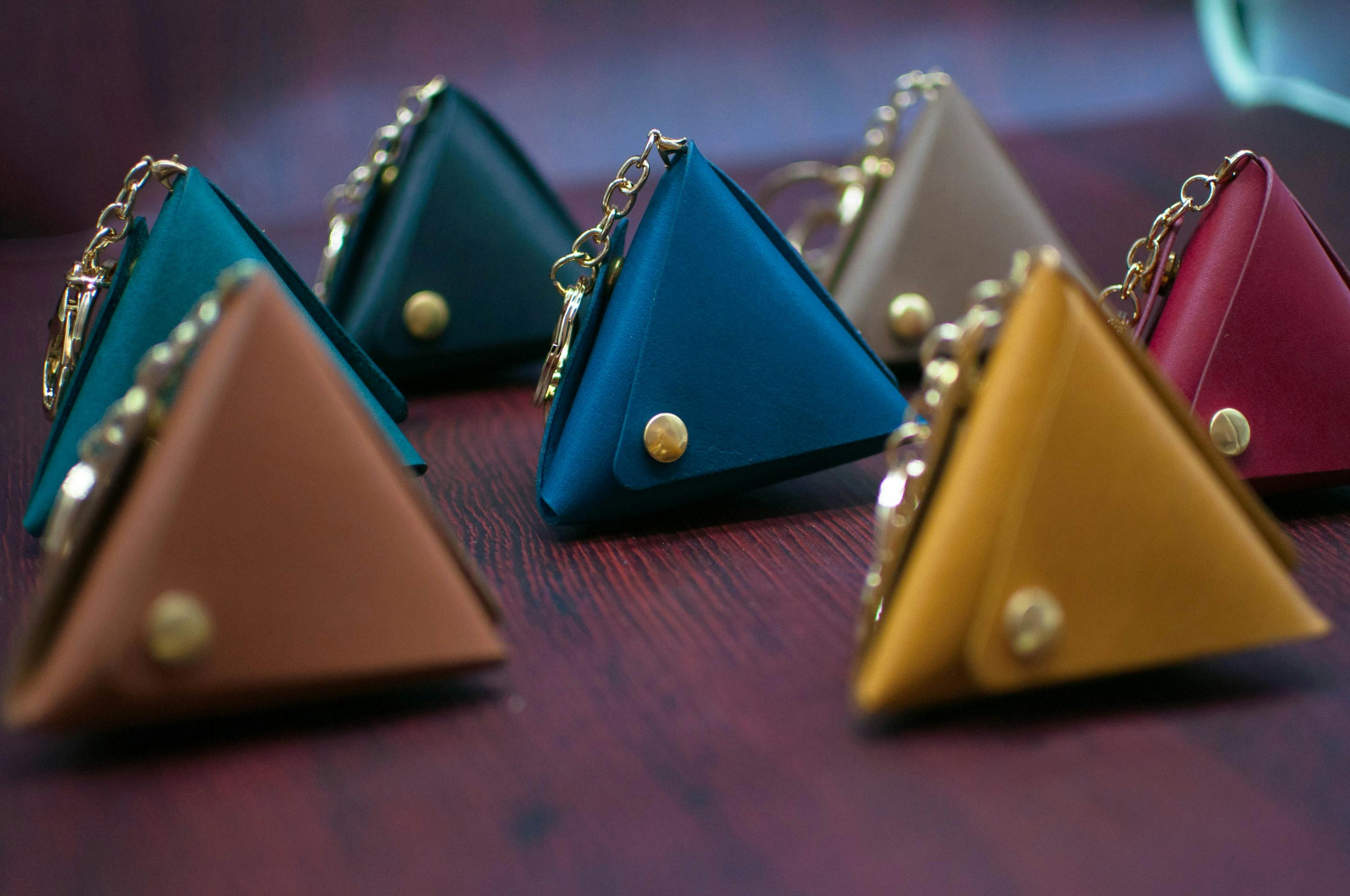Several small triangular pouches in various colors, each with a metal chain and button, arranged on a wooden surface.